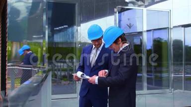 戴头盔的房地产开发商。 新的办公室建设。 自信的商人和建筑师在前面说话